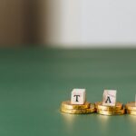 Pièces d'or empilées avec des blocs de bois épelant « TAX » sur un fond vert.