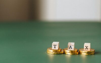 Pièces d'or empilées avec des blocs de bois épelant « TAX » sur un fond vert.