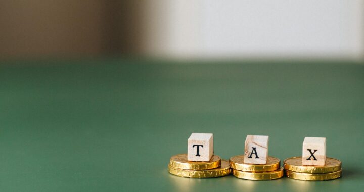 Pièces d'or empilées avec des blocs de bois épelant « TAX » sur un fond vert.