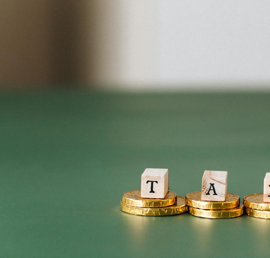 Pièces d'or empilées avec des blocs de bois épelant « TAX » sur un fond vert.