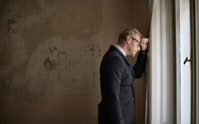 Un homme d'affaires inquiet en costume appuyé contre une fenêtre, exprimant son stress et son inquiétude.