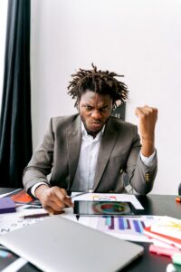 Un homme d'affaires montrant sa frustration face à des rapports et des graphiques à un bureau, affichant de fortes émotions.