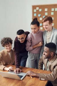 Un groupe diversifié de jeunes professionnels collaborant autour d'un ordinateur portable dans un environnement de bureau moderne.