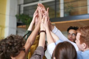 Un groupe de professionnels diversifiés célébrant le travail d'équipe avec un high-five à l'intérieur.