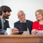 Groupe de trois personnes discutant autour d'une table avec une tablette et des tasses