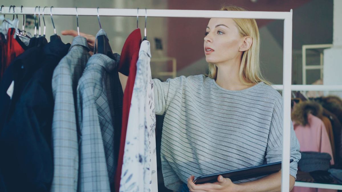 Femme blonde en boutique, inspecte des manteaux, livre à la main