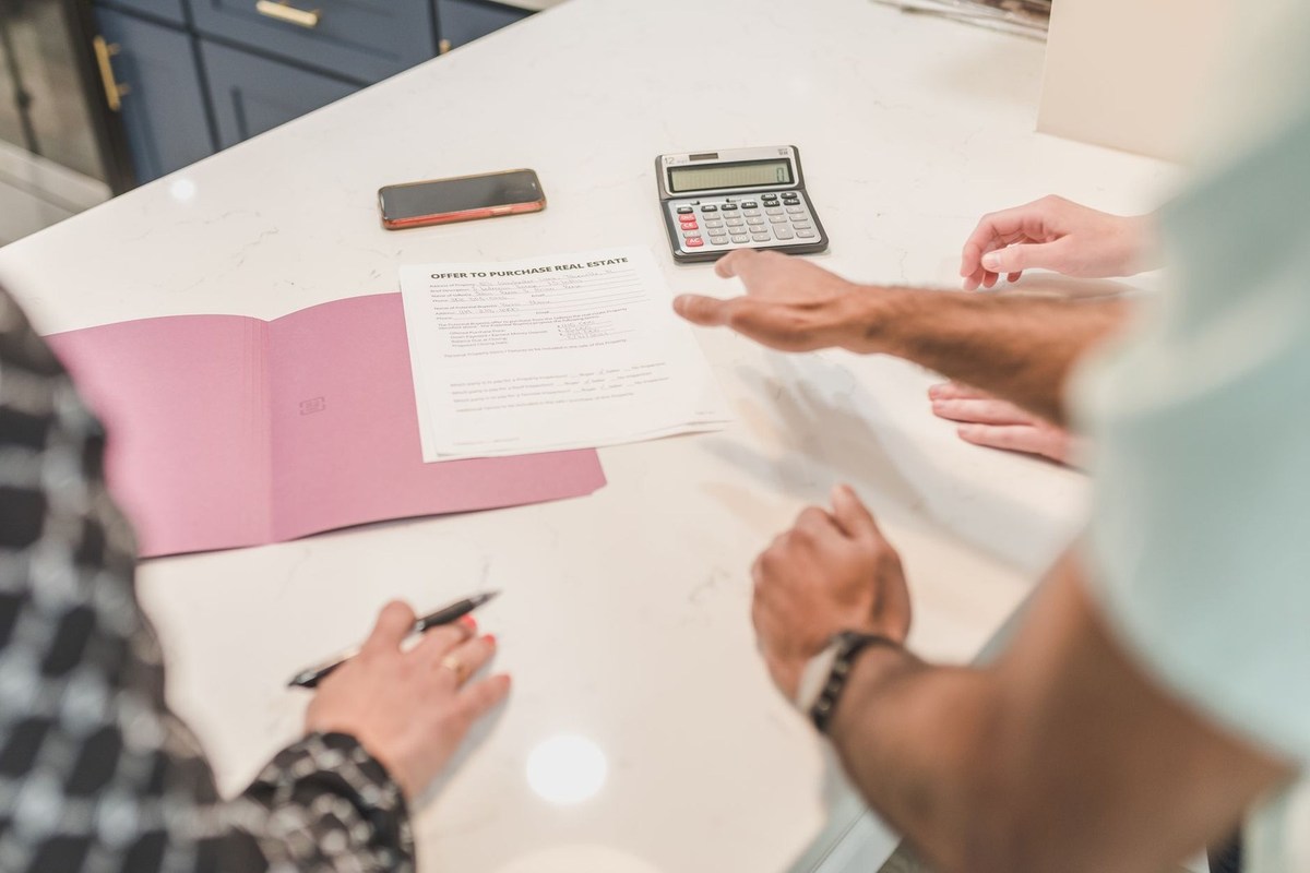 Deux personnes discutent autour d'un document, d'un livre et d'une calculatrice sur une table blanche Deux personnes discutent autour d'un document, d'un livre et d'une calculatrice sur une table blanche