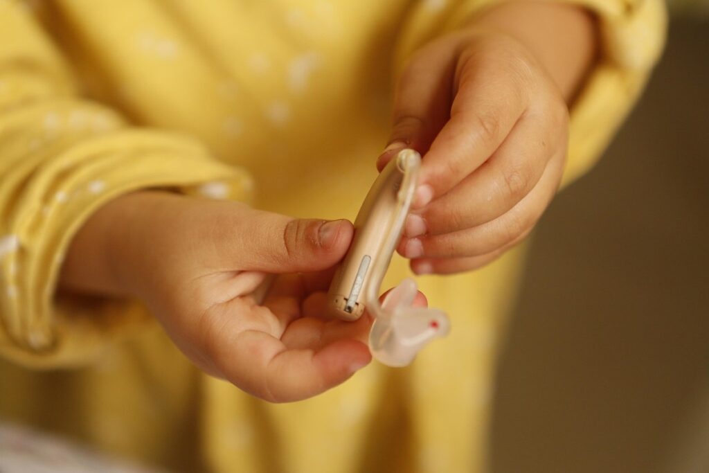 Un enfant tient un appareil auditif et son petit embout en main