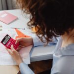 Femme utilisant une calculatrice rouge sur un bureau avec des documents et un agenda rose