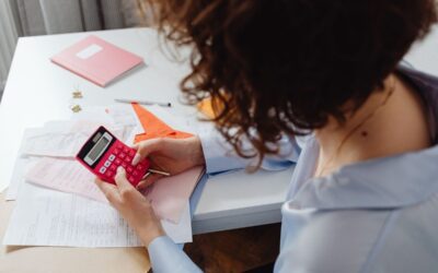 Femme utilisant une calculatrice rouge sur un bureau avec des documents et un agenda rose