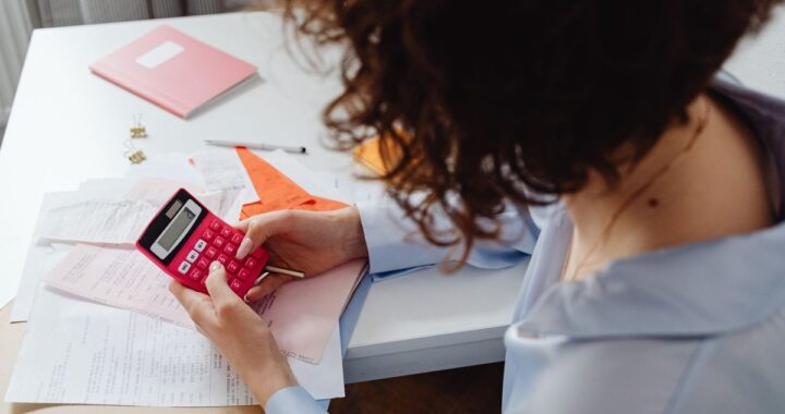Femme utilisant une calculatrice rouge sur un bureau avec des documents et un agenda rose