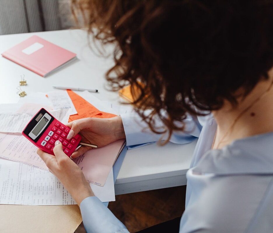 Femme utilisant une calculatrice rouge sur un bureau avec des documents et un agenda rose