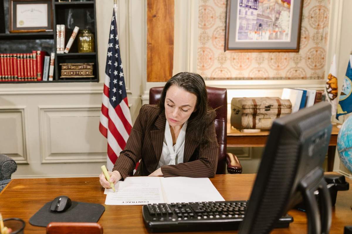Femme écrivant à un bureau avec un drapeau américain, un clavier et un écran devant elle Femme écrivant à un bureau avec un drapeau américain, un clavier et un écran devant elle