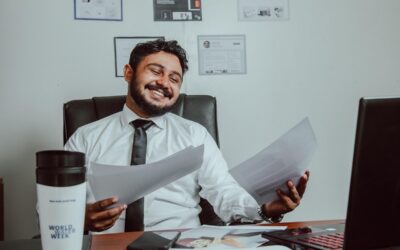 Un homme souriant tient des documents devant un ordinateur