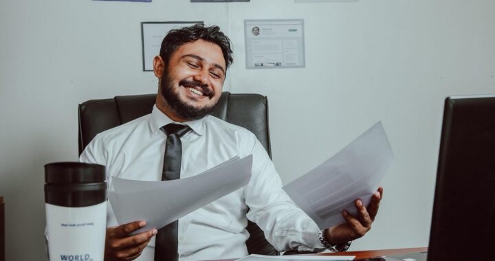 Un homme souriant tient des documents devant un ordinateur