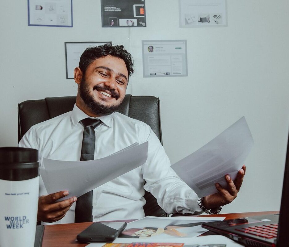 Un homme souriant tient des documents devant un ordinateur