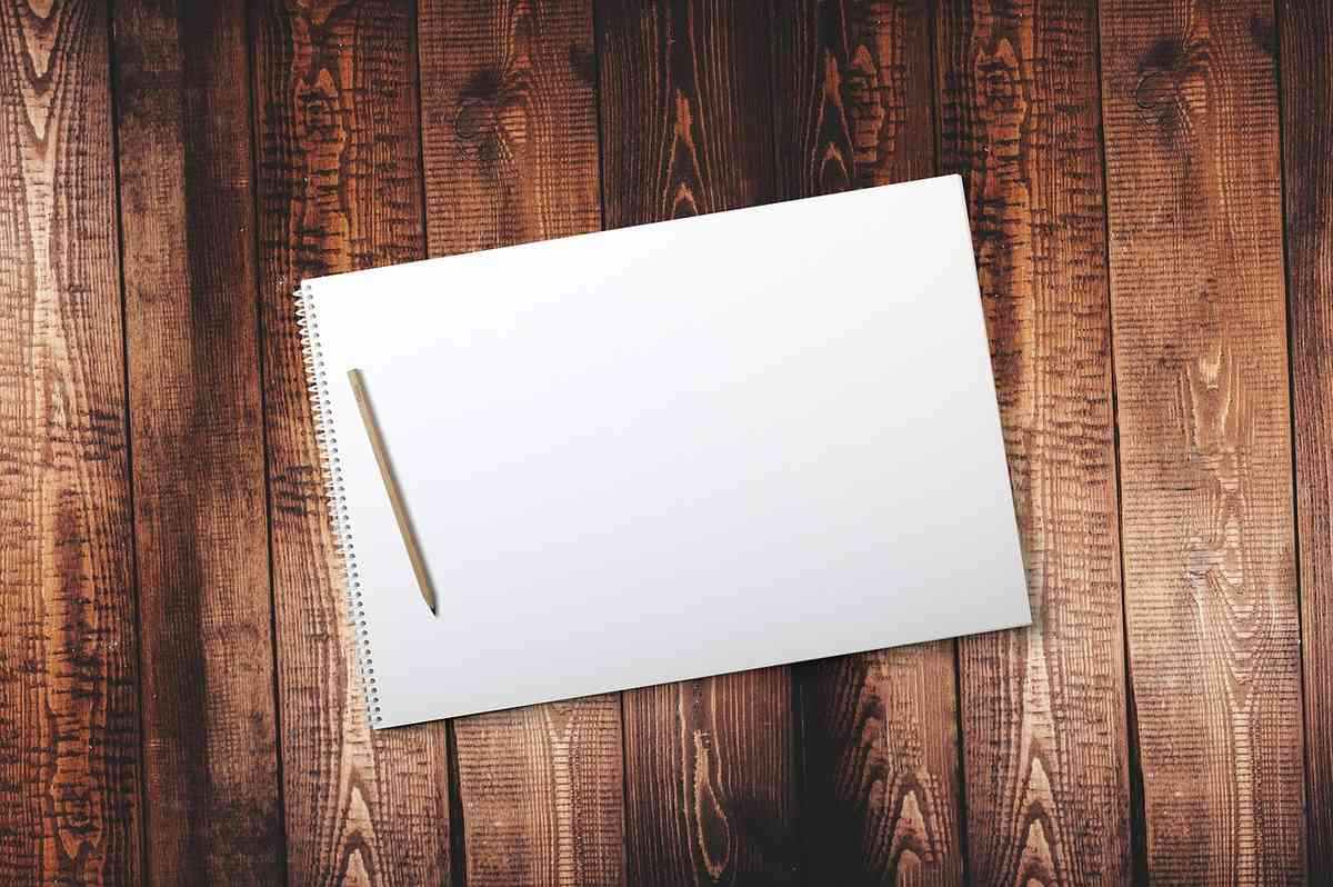 Cahier à spirale blanc ouvert avec un stylo, posé sur une surface en bois verni