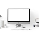 Bureau avec écran Apple, clavier, souris, lampe, tasse, théière et objets divers
