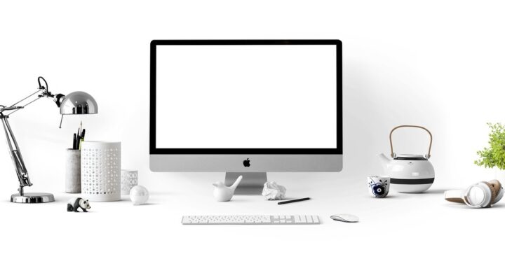 Bureau avec écran Apple, clavier, souris, lampe, tasse, théière et objets divers