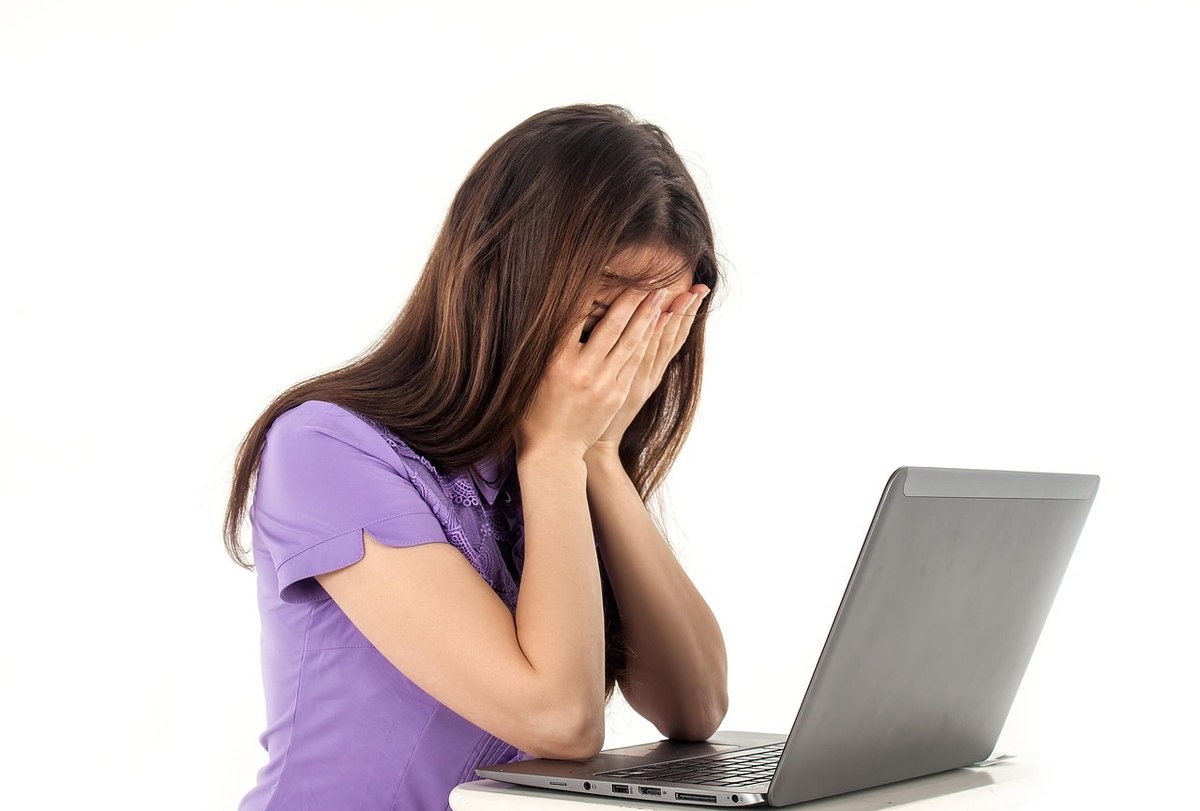 femme stressée devant ordinateur, mains sur visage, expression de désespoir