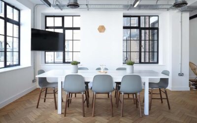 Une salle lumineuse avec table blanche, chaises, fenêtres et téléviseur mural