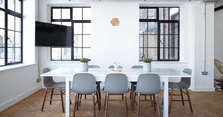 Une salle lumineuse avec table blanche, chaises, fenêtres et téléviseur mural