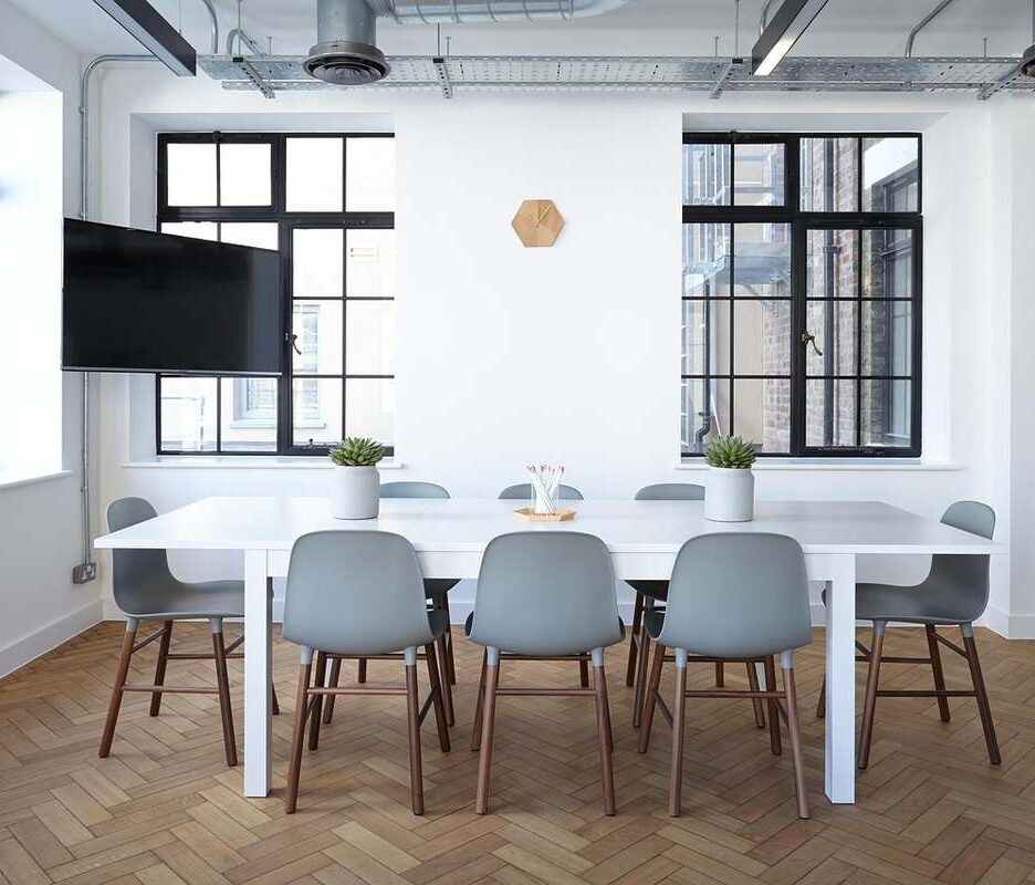 Une salle lumineuse avec table blanche, chaises, fenêtres et téléviseur mural