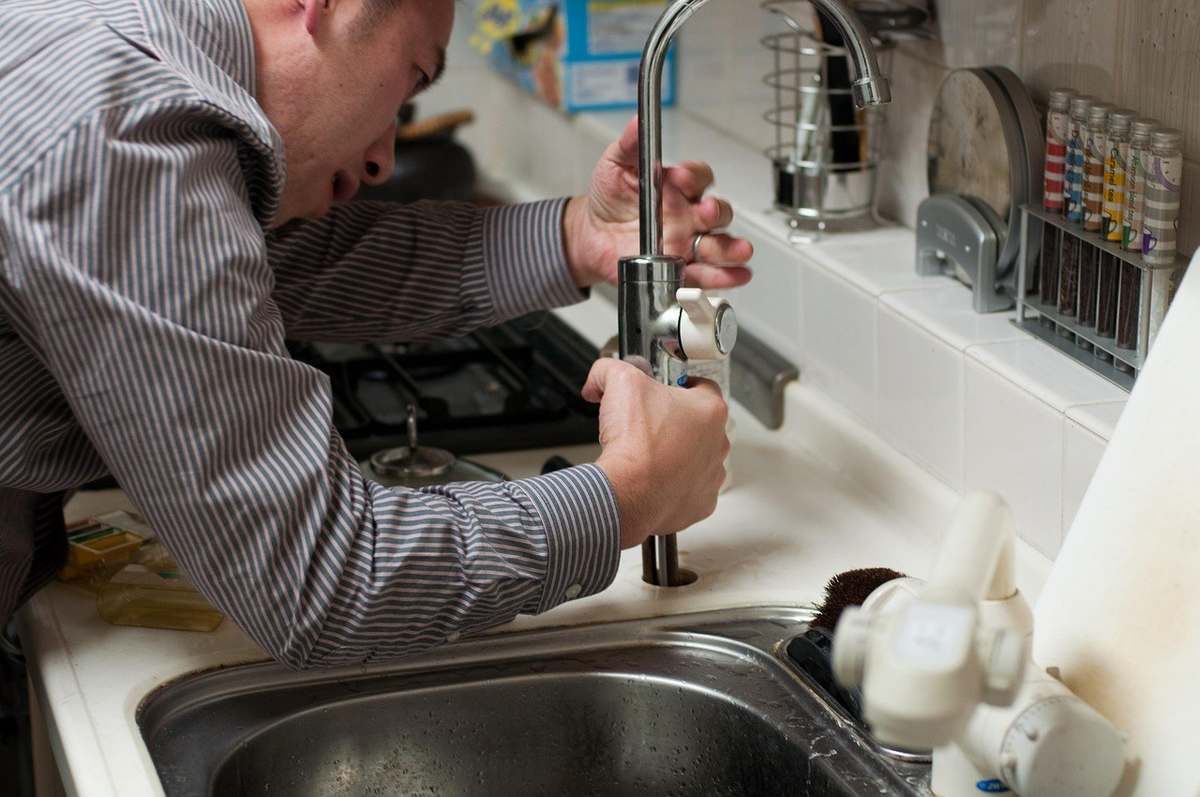 Homme ajuste un robinet dans une cuisine Homme ajuste un robinet dans une cuisine