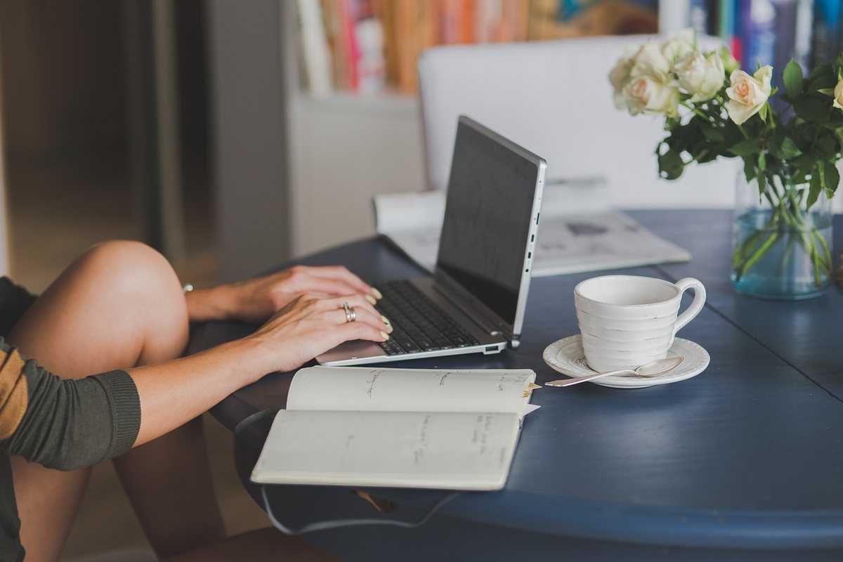 Une personne travaille sur ordinateur portable à table avec tasse et fleurs